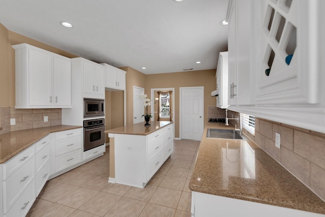 kitchen with light stone counters, light tile patterned flooring, stainless steel appliances, a kitchen island, and white cabinets