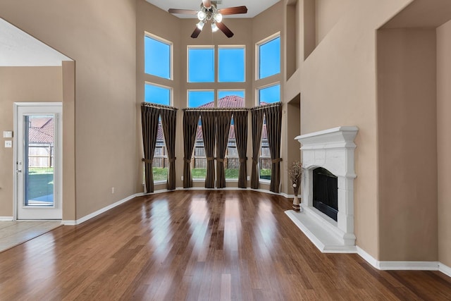 unfurnished living room featuring a fireplace with raised hearth, a towering ceiling, a ceiling fan, wood finished floors, and baseboards