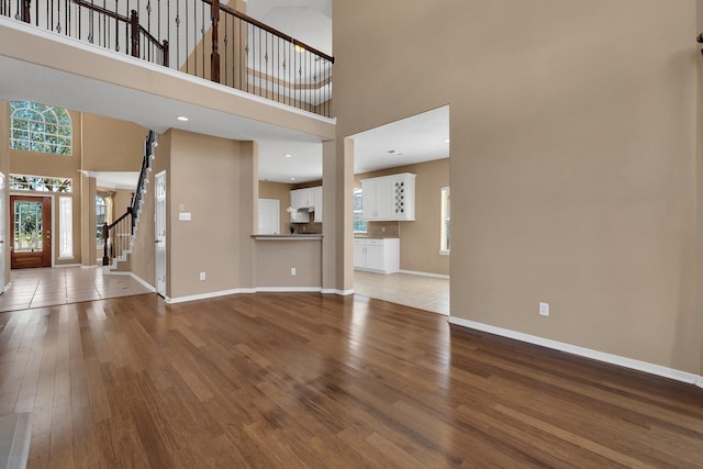 unfurnished living room featuring recessed lighting, a towering ceiling, wood finished floors, baseboards, and stairs