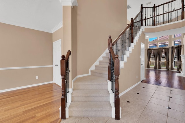 staircase featuring a high ceiling, crown molding, baseboards, and wood finished floors