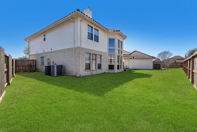 back of property with a storage shed, a fenced backyard, a chimney, an outbuilding, and a yard