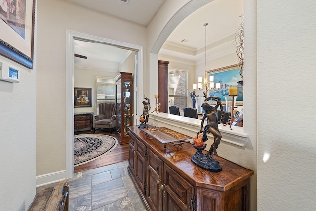 hall featuring arched walkways, stone finish floor, crown molding, and a textured wall