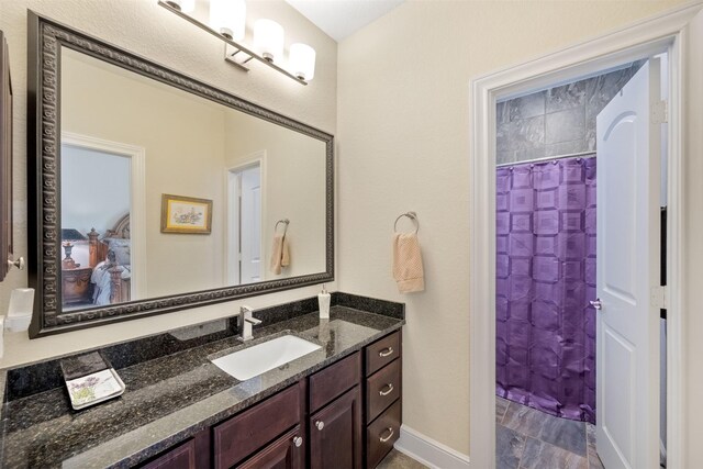 ensuite bathroom featuring vanity, a shower with curtain, baseboards, and connected bathroom