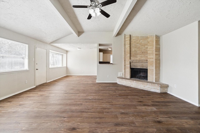 unfurnished living room with a textured ceiling, lofted ceiling with beams, wood finished floors, baseboards, and a brick fireplace