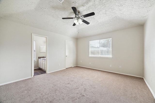 unfurnished bedroom with ceiling fan, a textured ceiling, connected bathroom, carpet flooring, and baseboards