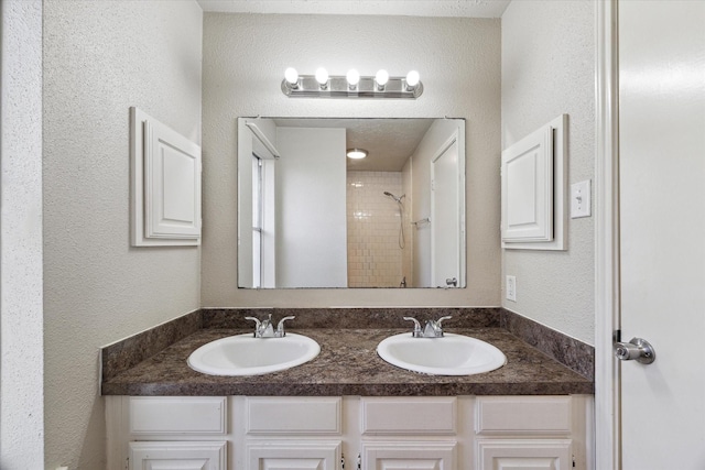 full bath with double vanity, a textured wall, a sink, and tiled shower