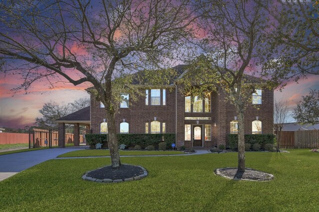 colonial house featuring a yard, brick siding, concrete driveway, and fence