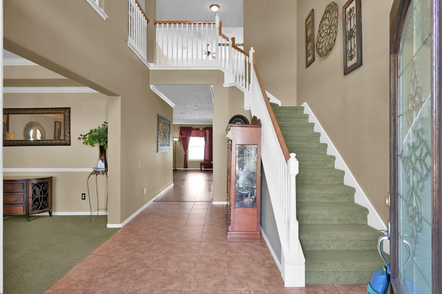 stairs featuring crown molding, baseboards, carpet floors, a towering ceiling, and tile patterned floors