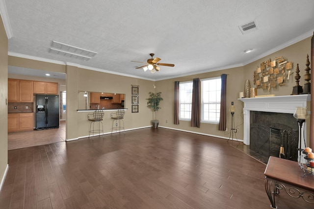 living room featuring wood finished floors, visible vents, a fireplace with flush hearth, ceiling fan, and crown molding