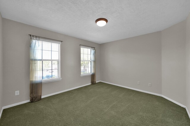 spare room with dark colored carpet, baseboards, and a textured ceiling