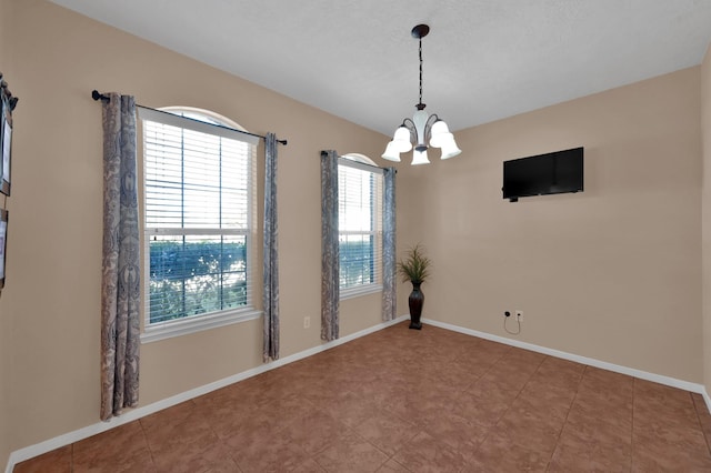 spare room featuring a chandelier and baseboards