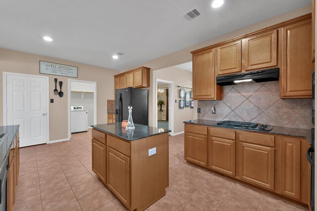 kitchen with visible vents, stainless steel gas cooktop, washer / dryer, under cabinet range hood, and black fridge