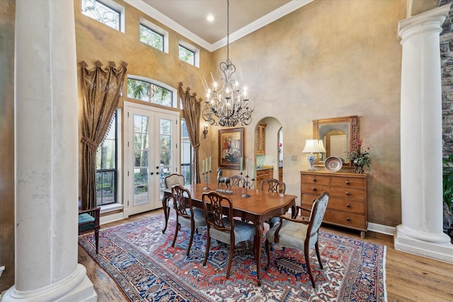 dining room featuring wood finished floors, baseboards, ornate columns, arched walkways, and crown molding