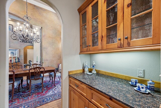 kitchen featuring dark stone countertops, decorative light fixtures, brown cabinetry, and arched walkways