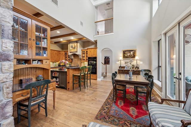 dining area with visible vents, light wood-style flooring, arched walkways, baseboards, and a towering ceiling