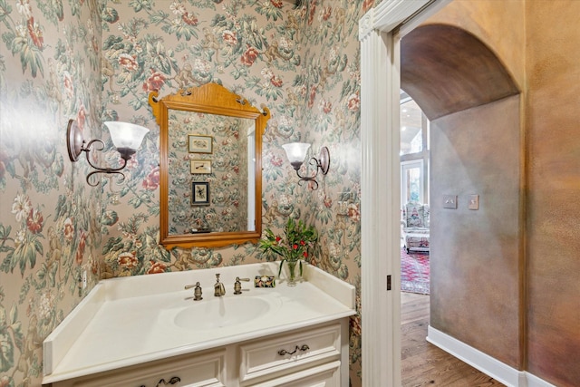 bathroom featuring wallpapered walls, vanity, wood finished floors, and baseboards