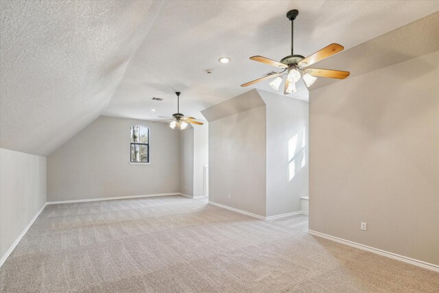 additional living space with visible vents, baseboards, light colored carpet, lofted ceiling, and a textured ceiling