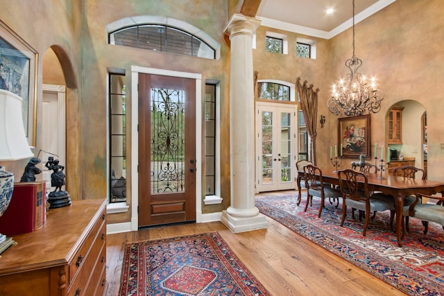 foyer with hardwood / wood-style floors, ornate columns, arched walkways, french doors, and a chandelier