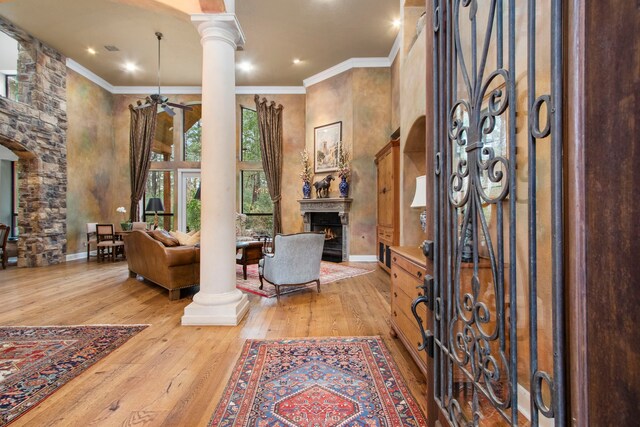 foyer entrance featuring a ceiling fan, wood-type flooring, a lit fireplace, crown molding, and decorative columns