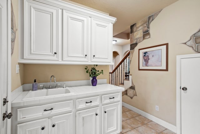 laundry area featuring a sink, baseboards, arched walkways, and light tile patterned flooring