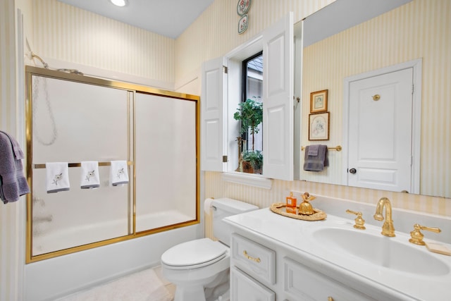 bathroom featuring toilet, wallpapered walls, vanity, and bath / shower combo with glass door