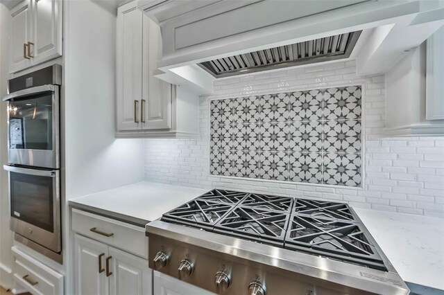 kitchen featuring gas stovetop, tasteful backsplash, double oven, white cabinets, and wall chimney range hood