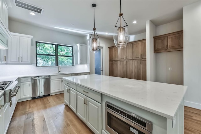 kitchen featuring light wood finished floors, visible vents, backsplash, appliances with stainless steel finishes, and a sink