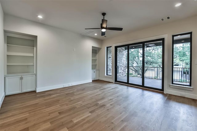 unfurnished room with light wood finished floors, visible vents, built in features, and baseboards