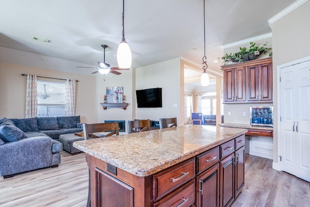 kitchen featuring decorative light fixtures, open floor plan, light wood-style floors, and ornamental molding