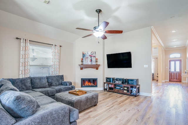 living area with a glass covered fireplace, lofted ceiling, baseboards, and light wood finished floors