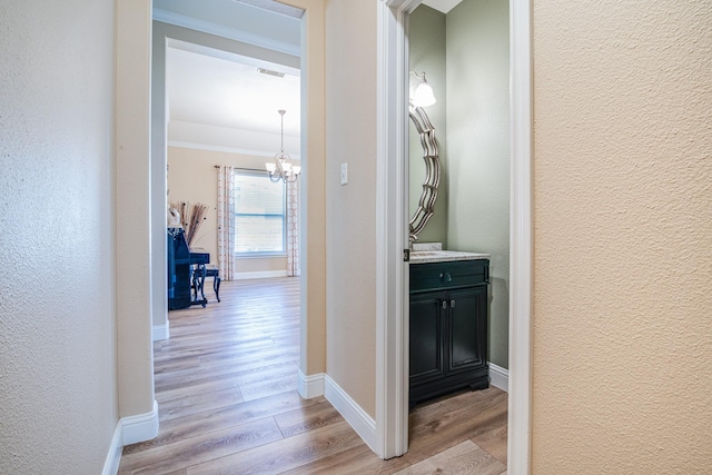 hall featuring light wood finished floors, baseboards, an inviting chandelier, and a textured wall