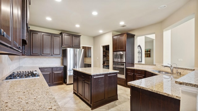 kitchen with light stone counters, dark brown cabinetry, stainless steel appliances, and a sink