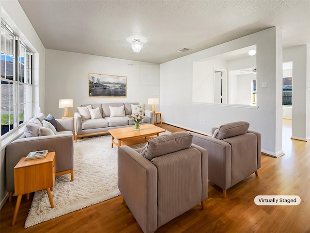 living room featuring visible vents, baseboards, a textured ceiling, and wood finished floors