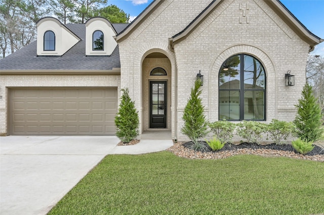 french country inspired facade with concrete driveway, brick siding, an attached garage, and a front lawn