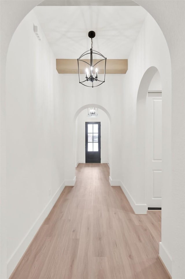 corridor featuring a chandelier, light wood-style flooring, and baseboards