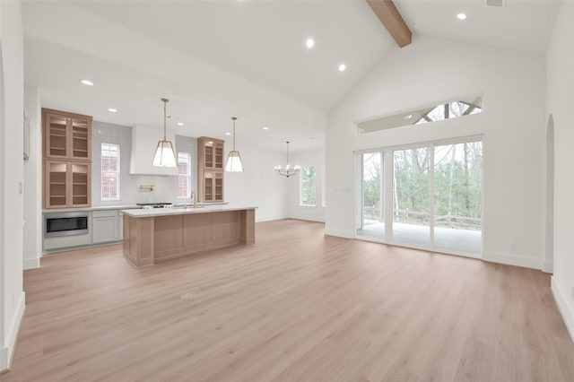 kitchen with open floor plan, light countertops, built in microwave, light wood finished floors, and beamed ceiling