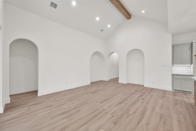 empty room featuring baseboards, visible vents, beamed ceiling, light wood-style floors, and high vaulted ceiling