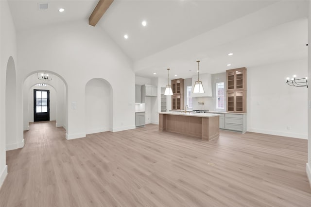 unfurnished living room with arched walkways, visible vents, light wood-type flooring, beam ceiling, and an inviting chandelier