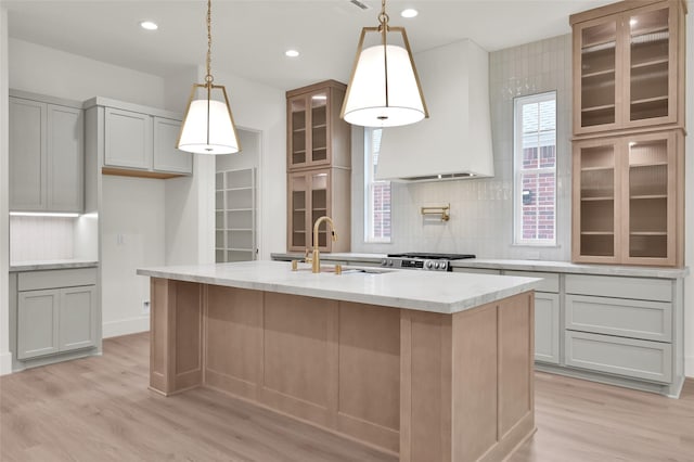 kitchen featuring a sink, light wood-style floors, wall chimney range hood, range, and a center island with sink