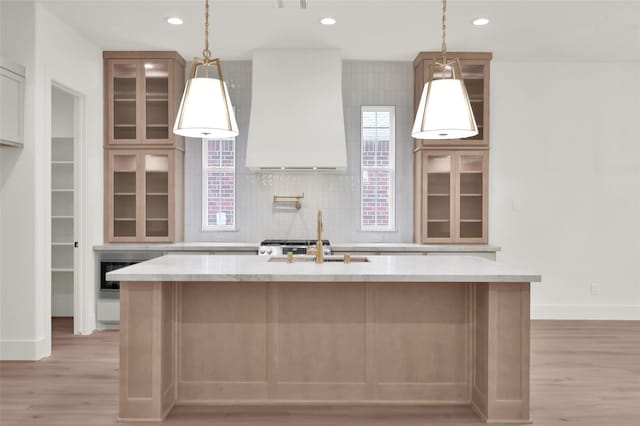 kitchen featuring a center island with sink, custom exhaust hood, recessed lighting, decorative backsplash, and a sink