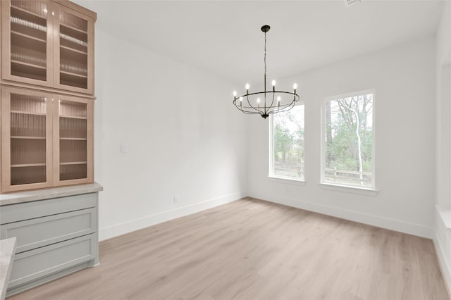 unfurnished dining area with light wood-style floors, baseboards, and an inviting chandelier