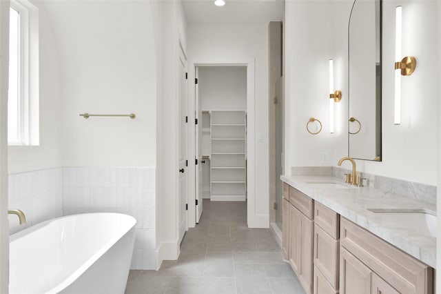 full bath featuring a sink, a freestanding bath, a spacious closet, tile patterned floors, and double vanity