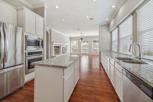 kitchen with stainless steel appliances, dark wood-type flooring, a kitchen island, a sink, and crown molding