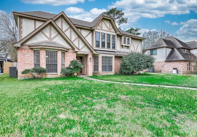 english style home with cooling unit, brick siding, a front lawn, and roof with shingles