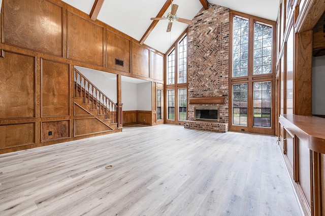 unfurnished living room with light wood finished floors, ceiling fan, beamed ceiling, a brick fireplace, and a decorative wall