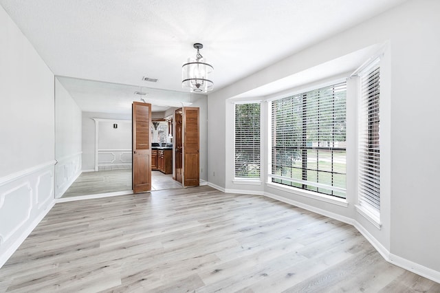 unfurnished dining area with visible vents, a wainscoted wall, light wood-style floors, a chandelier, and a decorative wall