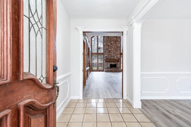 foyer with light tile patterned floors, a textured ceiling, a wainscoted wall, a fireplace, and ornate columns