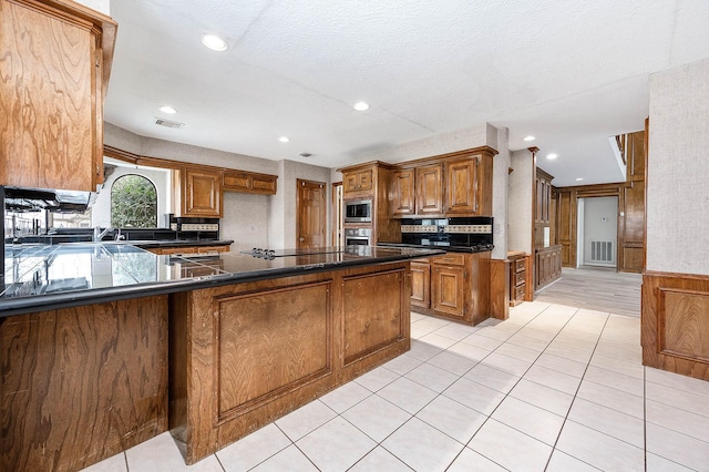 kitchen featuring stainless steel appliances, visible vents, decorative backsplash, brown cabinetry, and dark countertops