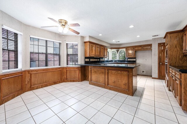 kitchen with a peninsula, brown cabinetry, dark countertops, and a wealth of natural light