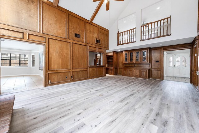 unfurnished living room featuring light wood finished floors, visible vents, a decorative wall, ceiling fan, and wood walls